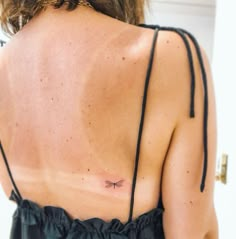 the back of a woman's dress with a dragonfly tattoo on her left shoulder