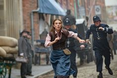 a woman is running down the street with other people behind her and another man in uniform