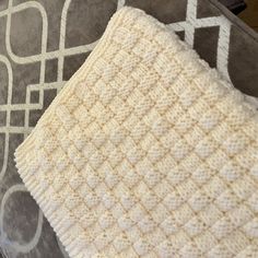 a close up of a white and gray blanket on a bed with pillows in the background