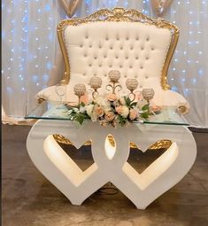 a white and gold love seat with flowers on the table in front of a backdrop