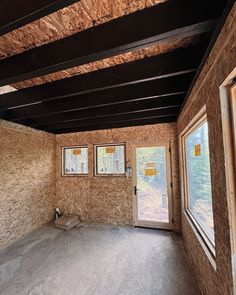 an empty room with boarded up walls and two windows in the wall, some missing insulation