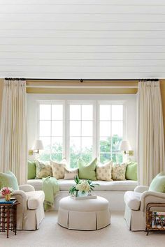 a living room filled with white furniture and lots of green pillows on the windowsill