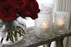 three white vases with red roses in them sitting on a table next to candles