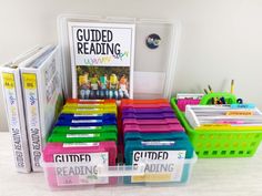 several different colored books in a plastic container and some children's reading materials on the table