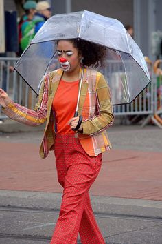 a woman walking down the street with an umbrella in her hand and clown makeup painted on her face