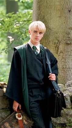 a young man dressed in a harry potter costume standing next to a tree and trunk