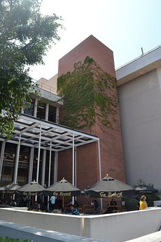 people sitting at tables in front of a building with umbrellas on the outside wall