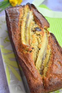 a loaf of banana bread sitting on top of a white plate next to yellow flowers