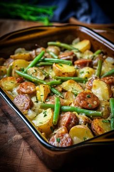 a casserole dish filled with potatoes, green beans and sausage on a wooden table