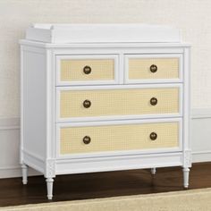 a white dresser with yellow drawers and wicker baskets on the bottom drawer, against a beige wall