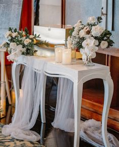 a white table with candles and flowers on it in front of a mirror next to a rug