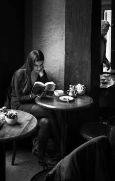 a woman sitting at a table reading a book