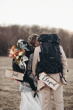 a man and woman are standing in a field with backpacks on their backs, kissing