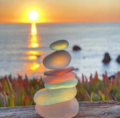 a stack of rocks sitting on top of a wooden table next to the ocean at sunset