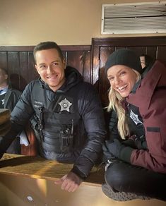 a man and woman sitting next to each other in front of a wooden bench with two police officers on it