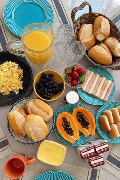 a table topped with blue plates and bowls filled with food next to breads, fruit