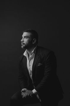 a black and white photo of a man in a tuxedo sitting on a stool