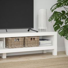 a flat screen tv sitting on top of a white shelf next to a potted plant