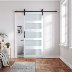 a bedroom with white walls and wooden floors has a sliding glass door that leads to the bathroom