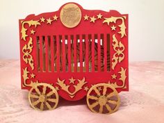 a red and gold card with wooden wheels on a pink tableclothed surface,