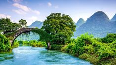 a bridge over a river with mountains in the backgrouds and green trees