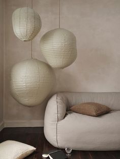 three white paper lanterns hanging from the ceiling above a couch and table with silverware on it