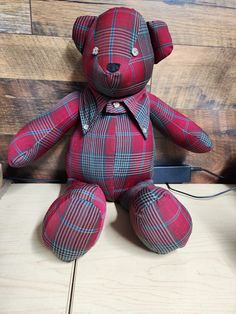 a red plaid teddy bear sitting on top of a wooden floor next to a wall