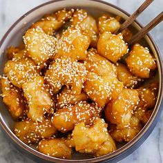 a bowl filled with sesame seed chicken and two chopsticks sticking out of it