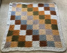 a crocheted blanket is laying on the floor in front of a carpeted area