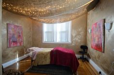 a bed sitting under a window in a bedroom next to a chair and rug on top of a hard wood floor