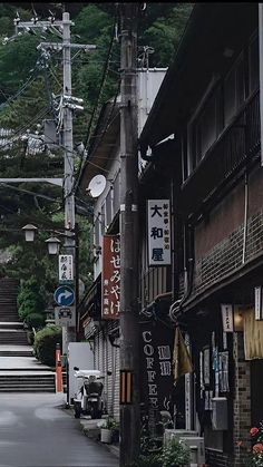 an alley way with many signs on the buildings and stairs leading up to trees in the background