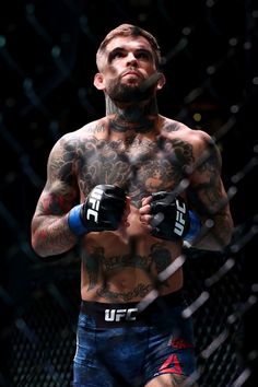 a man with tattoos on his chest holding two boxing gloves in front of a chain link fence