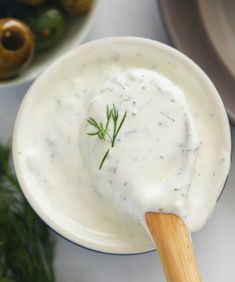 a white bowl filled with ranch dressing next to olives