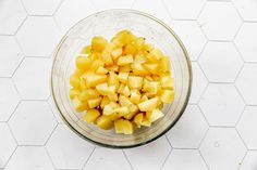 a glass bowl filled with chopped pineapple on top of a white tiled countertop