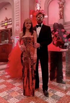 a man and woman standing next to each other in front of a pink wall with flowers