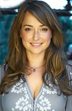 a woman with long brown hair wearing a gray shirt and white flowers on it's chest