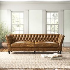 a brown leather couch sitting on top of a wooden floor next to a rug and windows