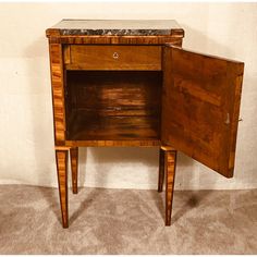 an old wooden cabinet with marble top and legs on carpeted floor next to white wall