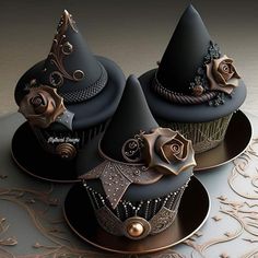 three cupcakes decorated with black and gold decorations on top of a silver plate