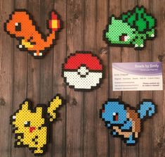 four pixellated pokemon magnets are displayed on a wooden surface with a business card in the foreground