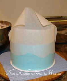 a blue and white cake sitting on top of a wooden table next to a metal bowl