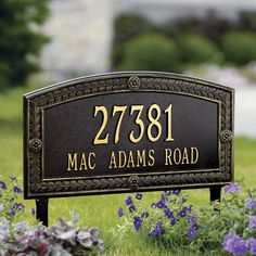 a brown sign sitting in the grass next to purple and white flowers on top of green grass