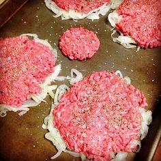 four hamburger patties cooking in a pan with onions and seasoning on top, ready to be cooked