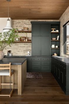 a kitchen with dark green cabinets and wood flooring on the walls, along with a wooden dining table