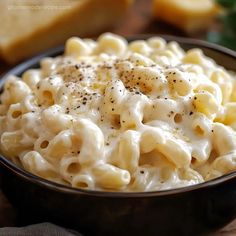 a bowl filled with macaroni and cheese on top of a wooden table next to bread