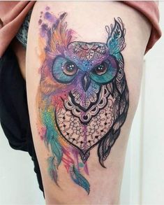 an owl tattoo on the thigh with colorful feathers and watercolor paint splatters