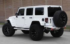 a white jeep parked in front of a brick building with large tires on it's tires