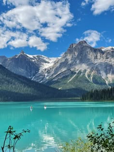 two boats floating on top of a blue lake surrounded by trees and mountains in the background