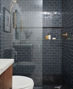 a white toilet sitting in a bathroom next to a walk in shower and tiled walls