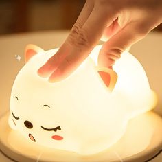 a person touching the light on top of a cat shaped nightlight that is sitting on a table